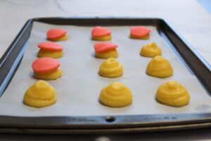 Unbaked choux pastry with pink craquelin on a pan on a marble countertop