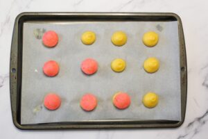 Unbaked choux pastry with pink craquelin on a pan on a marble countertop